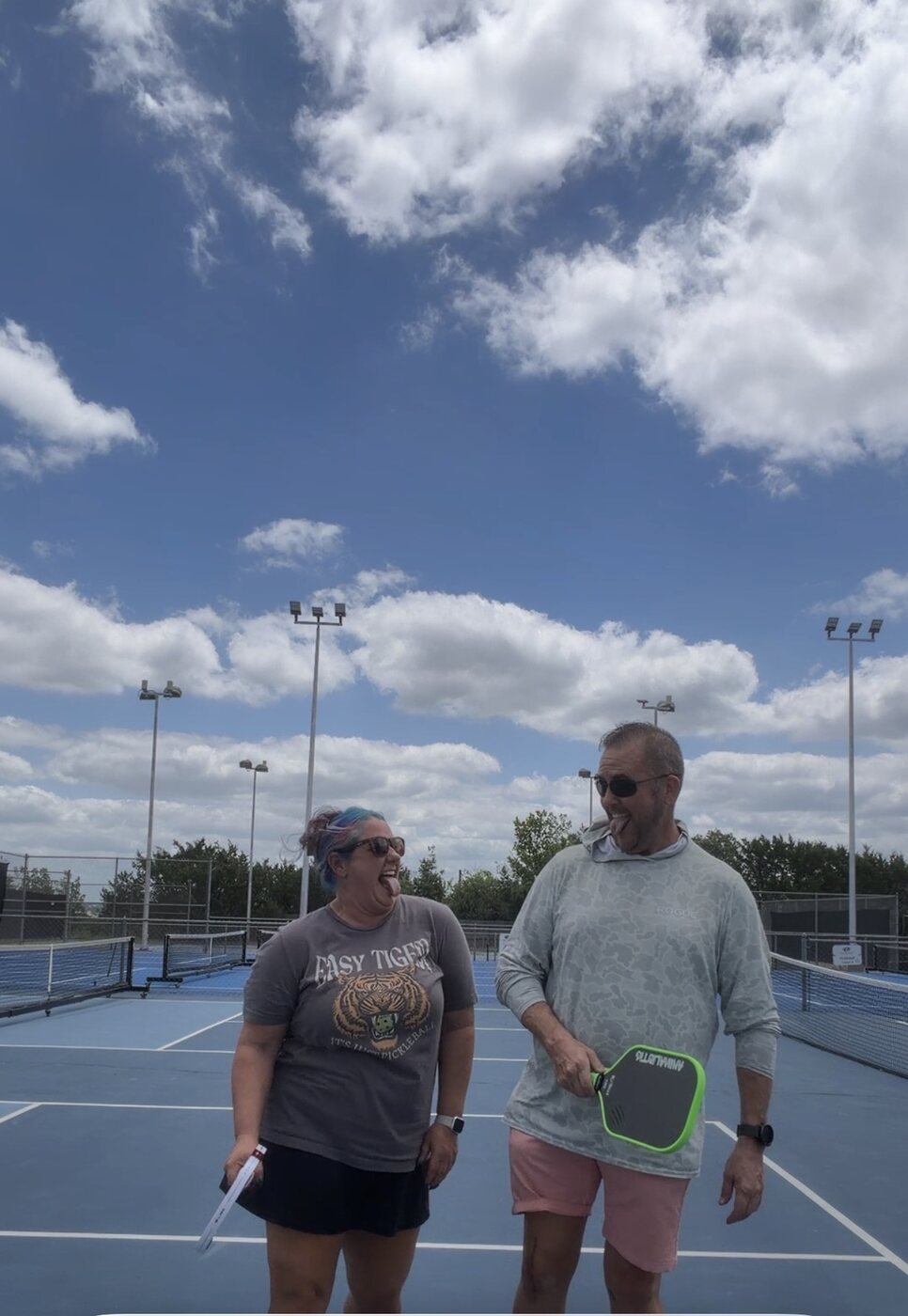 Two people laughing together on an outdoor pickleball court